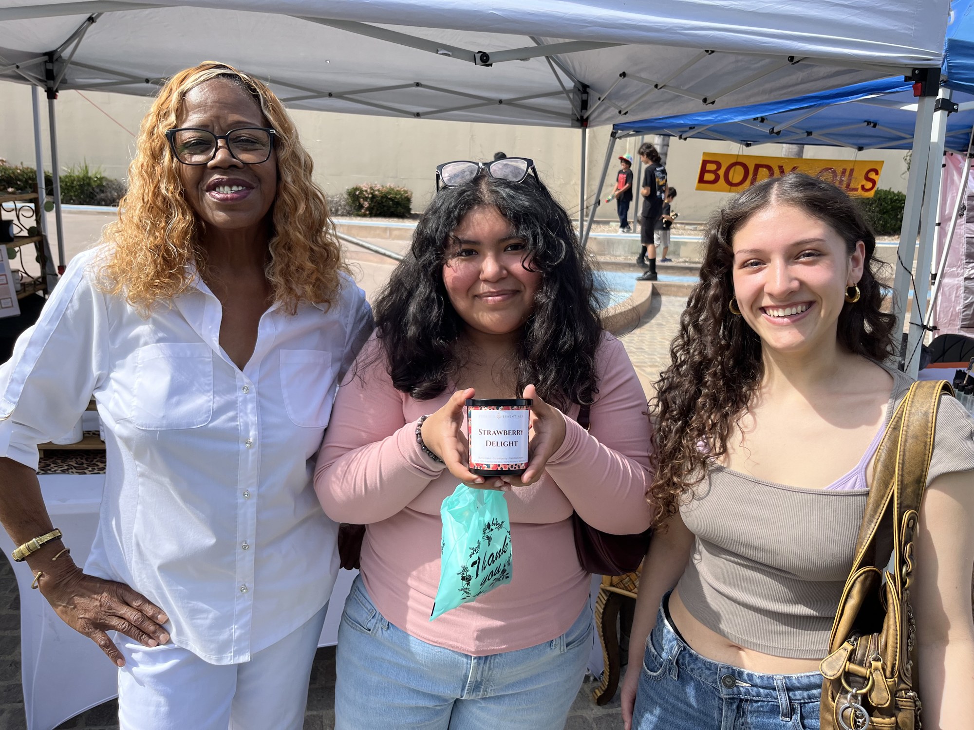 Two young women with Debbie holding a Strawberry Delight candle at the booth