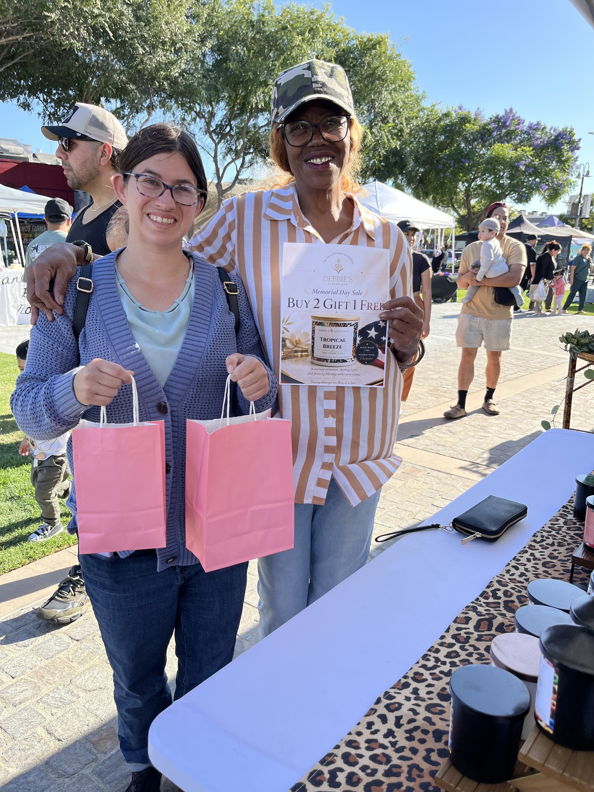 A customer holding two pink Debbie's Essentials gift bags next to Deborah at the Memorial Day sale
