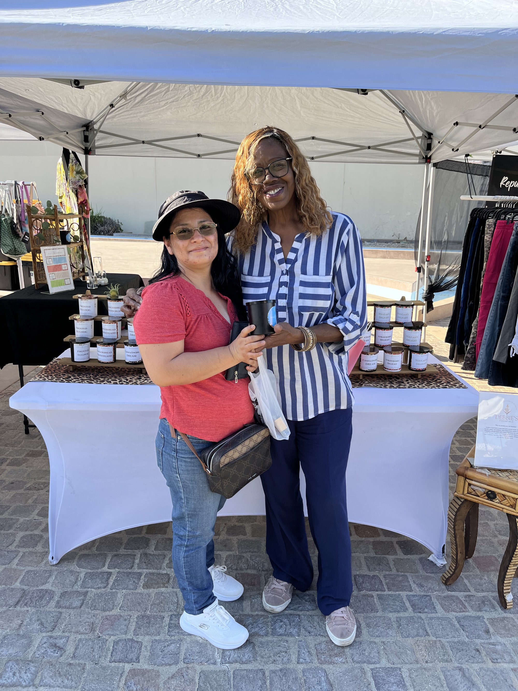 A woman in a red top holding a Debbie's Essentials candle next to Deborah at the booth