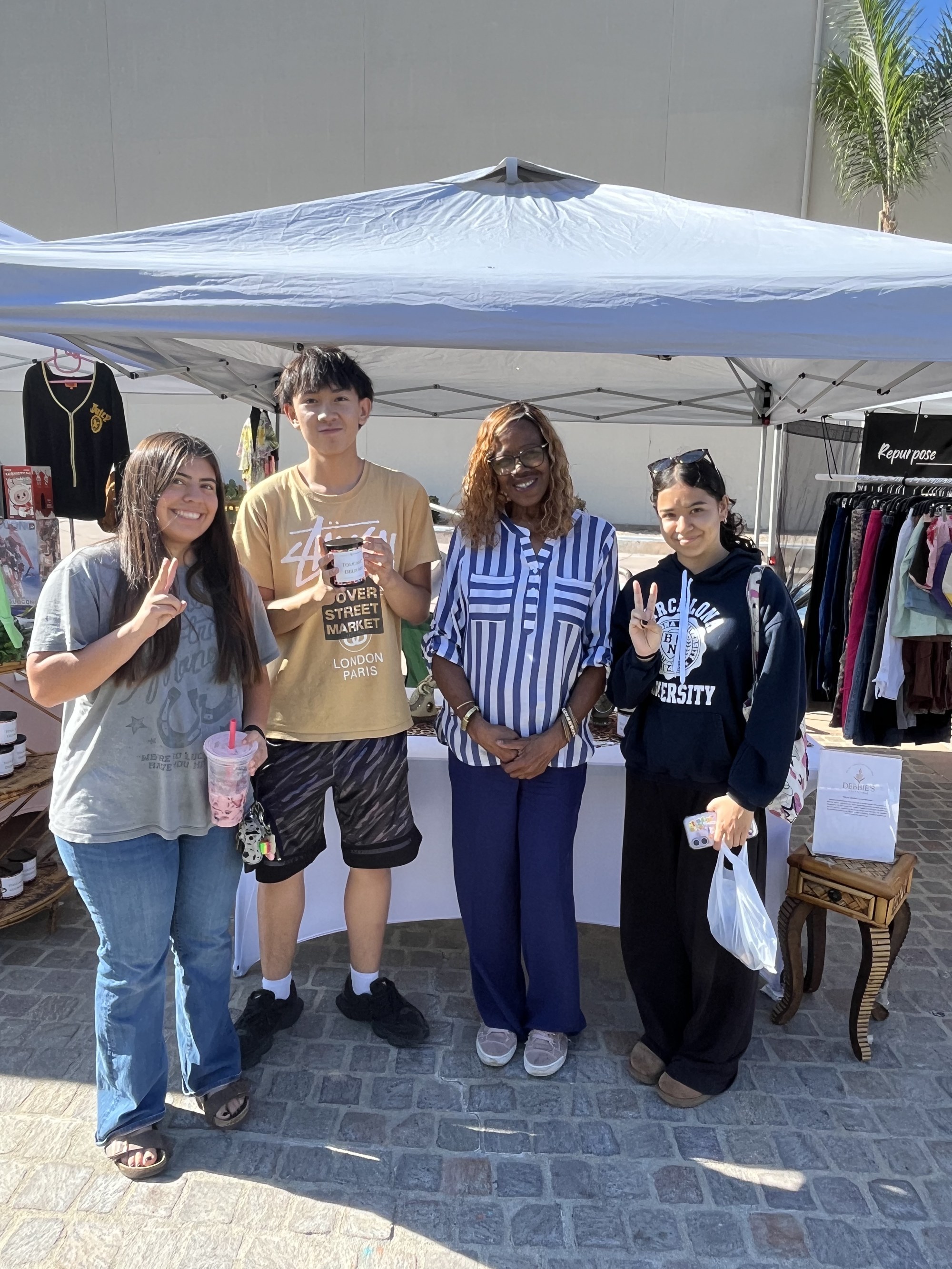 Four young customers posing with Deborah, one holding a Toucan's Delight candle at the market booth